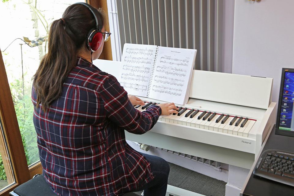 Adolescente jouant du piano à l'aide d'une partition posée sur celui-ci