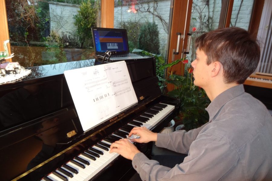 Jeune homme en train de jouer du piano devant une partition et un ordinateur